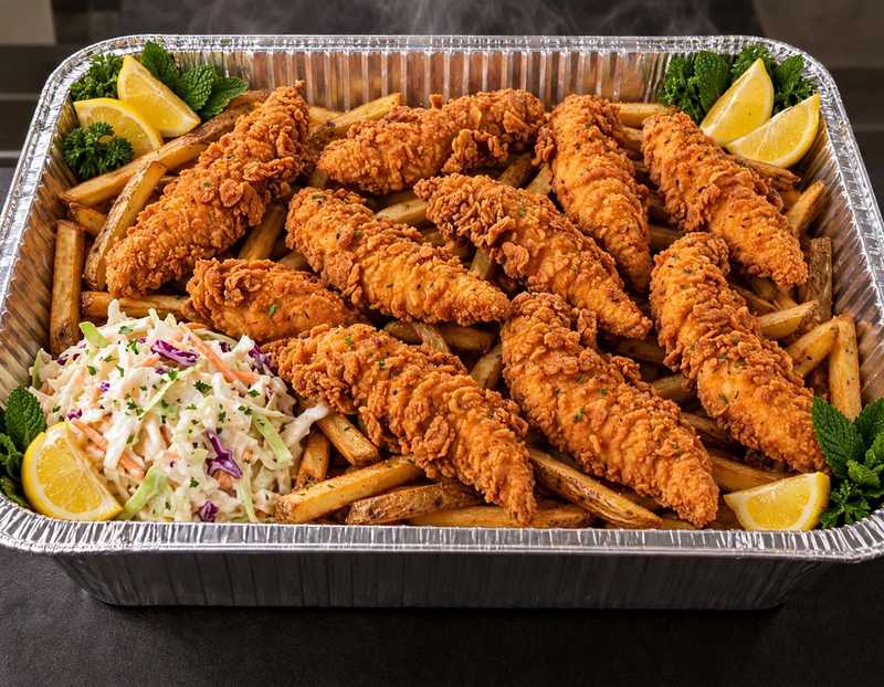 Catering pan of crispy chicken tenders over fries with coleslaw and lemon garnish